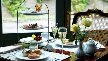A three-tiered tea service set on a table with plates of pastries, a vase with flowers, and a teapot.