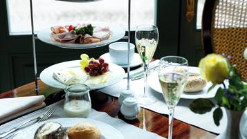Een drijvende etagère met verschillende soorten eten, een glas witte wijn en een vaas met bloemen op een tafel.