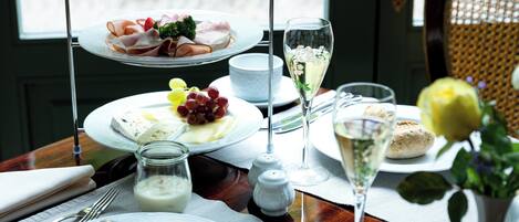 Una bandeja de tres niveles con diversas comidas, una copa de vino blanco y un florero con flores sobre una mesa.