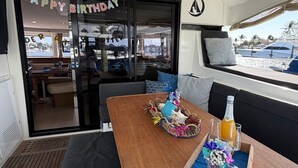 Interior de un barco con una mesa de madera, asientos y vistas al exterior.