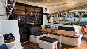Interior de un yate con una zona de estar, una mesa y vistas al exterior.