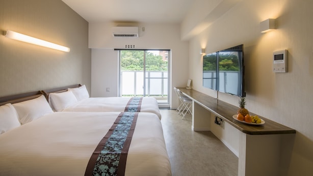 Een hotelkamer met een groot bed, een bureau met een fruitmand, een flatscreen-tv en een schuifdeur naar een balkon.
