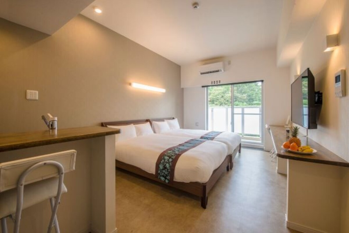 Une chambre d’hôtel équipée d’un lit, d’un bureau, d’une chaise, d’une télévision et d’une fenêtre donnant sur un paysage verdoyant.