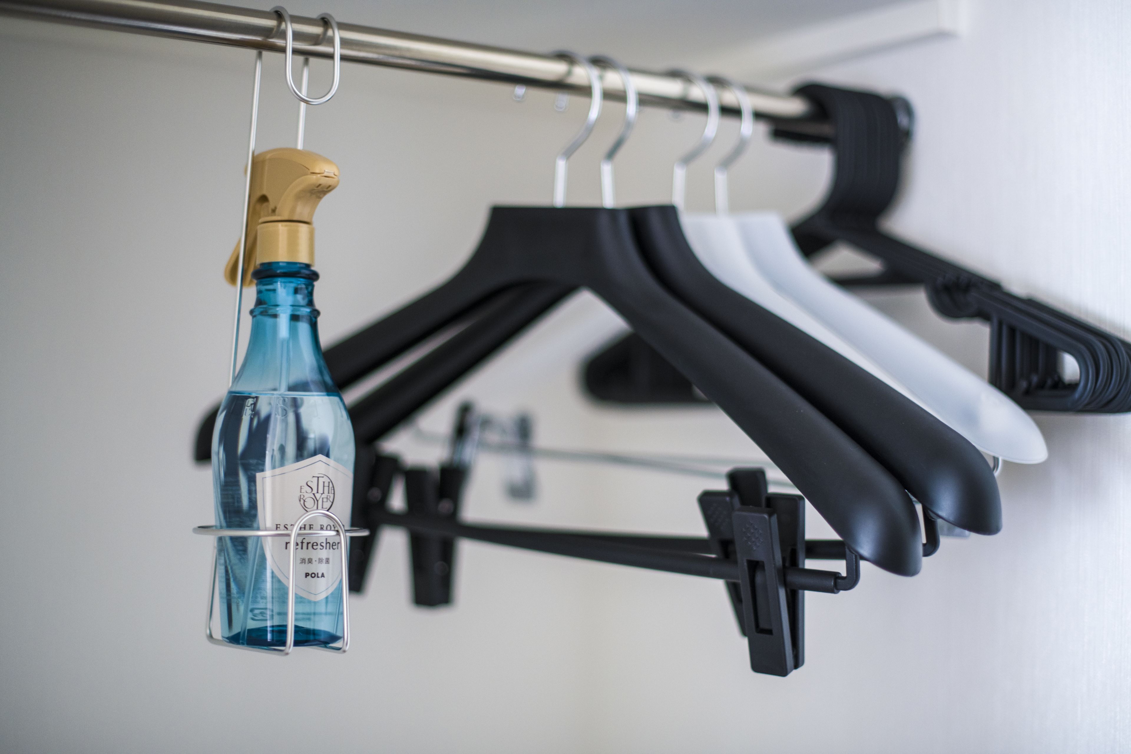 A bottle of blue liquid hanging from a metal rod, with black and white hangers in the background.