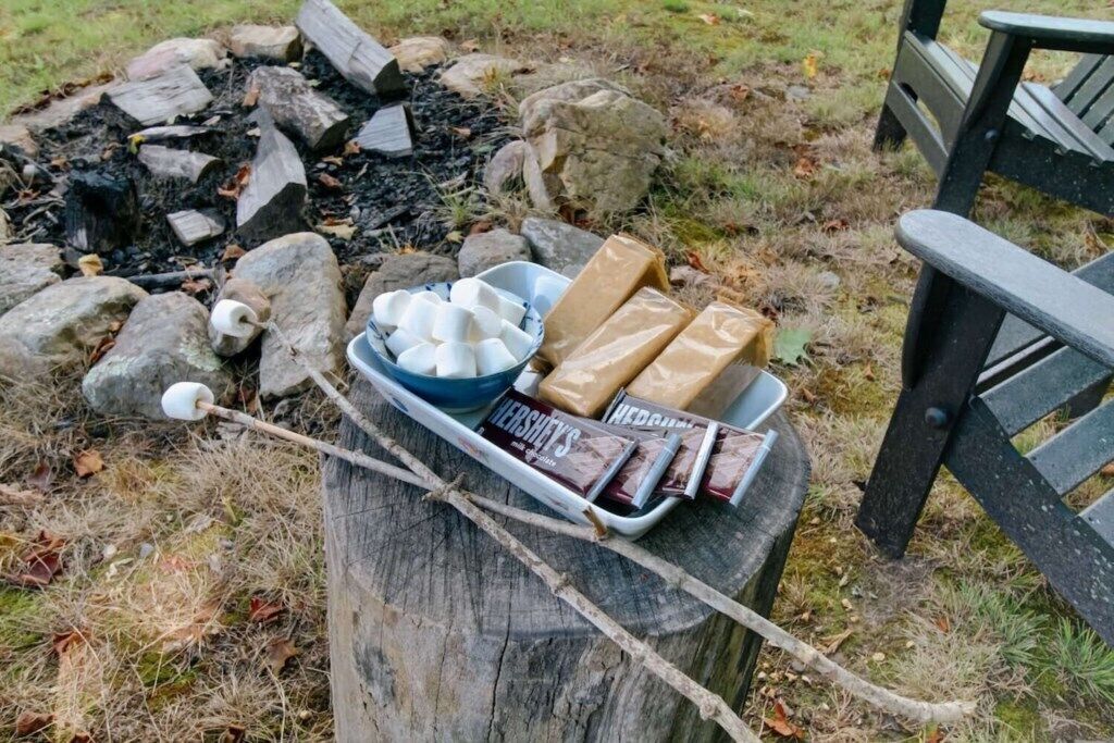 A picnic setup with marshmallows, Hershey's chocolate bars, and a bowl of marshmallows on a wooden stump.