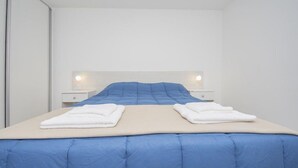 Uma cama bem arrumada com um edredom azul e duas toalhas brancas dobradas sobre ela.