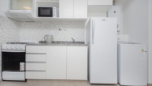Uma cozinha moderna com armários brancos, micro-ondas embutido, fogão e geladeira.