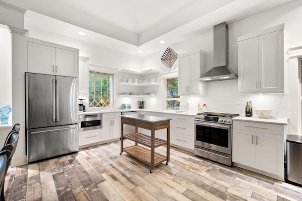 Una cocina moderna con electrodomésticos de acero inoxidable, armarios blancos y piso de madera.