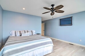 Un dormitorio con cama, ventilador de techo, televisor montado en la pared y una puerta que da a otra habitación.