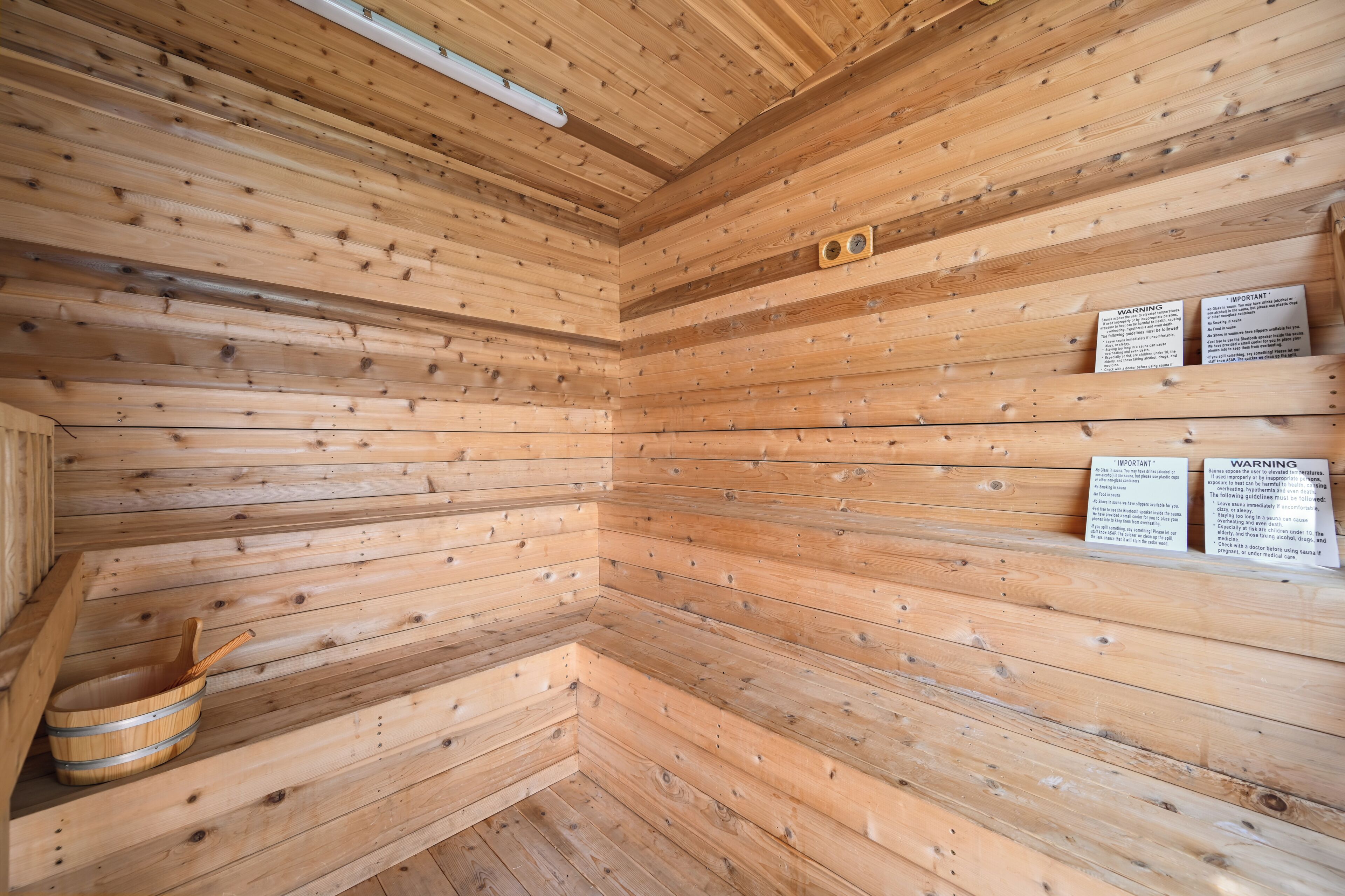 A wooden sauna room with slatted walls, a wooden bucket, and informational signs.