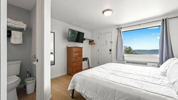 Un dormitorio con cama, televisión, cómoda, ventana con cortinas y vista al exterior.