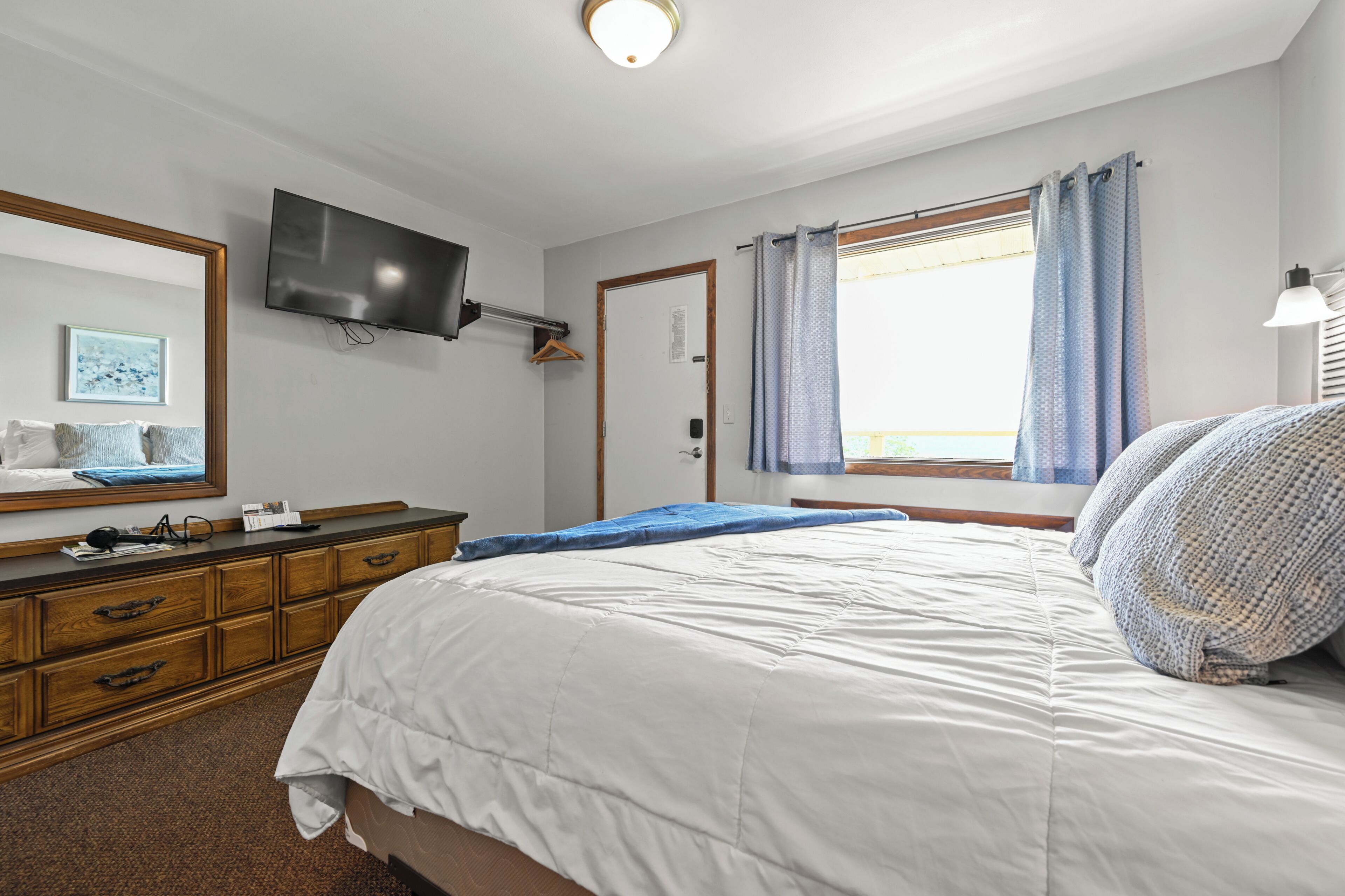 Un dormitorio con cama, cómoda, televisor y ventana con cortinas.