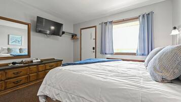 Un dormitorio con cama, cómoda, televisor y ventana con cortinas.