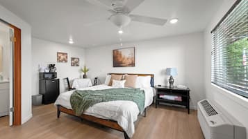 A modern bedroom with a bed, bedside table, lamp, and a view of the outdoors through a window.