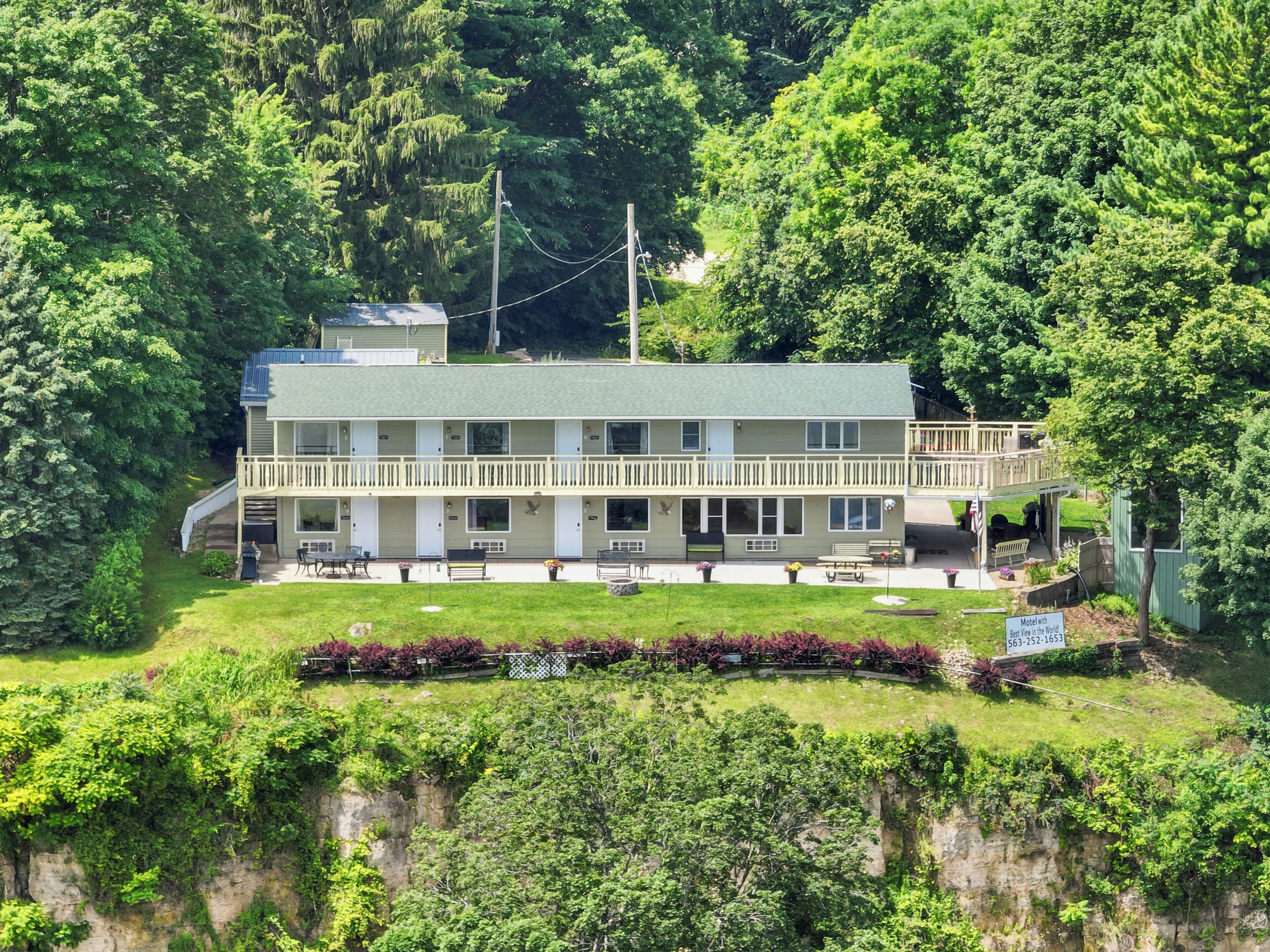 A motel with a two-story structure, outdoor seating, and a view of the surrounding greenery.