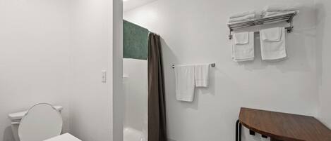 Een badkamer met een witte wastafel, toilet, douche met gordijn en een houten bankje.