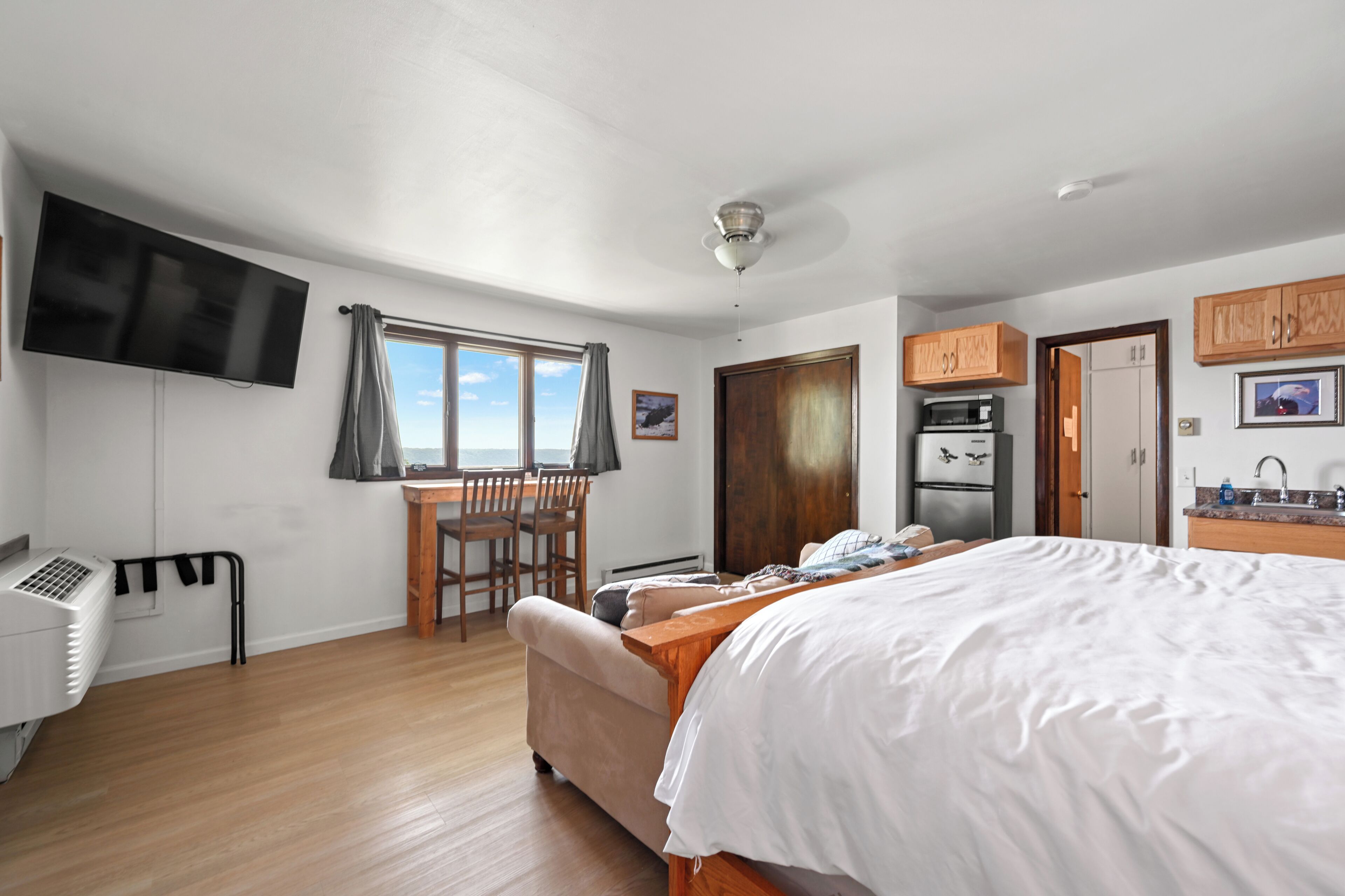 Un dormitorio moderno con una cama grande, un escritorio con sillas, un televisor y una kitchenette.