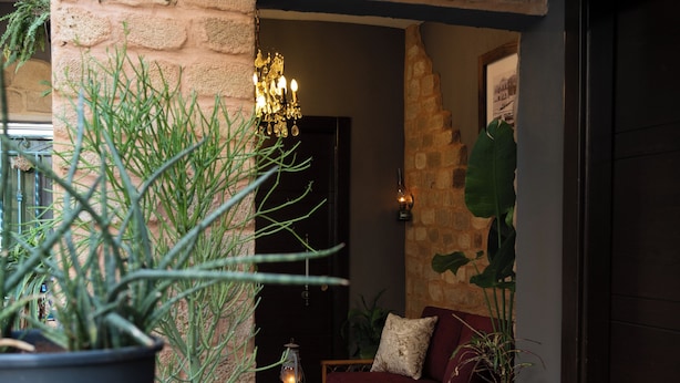 A cozy outdoor seating area with a brick archway, potted plants, and a wooden table with a lantern. - InnTown (Tyre)