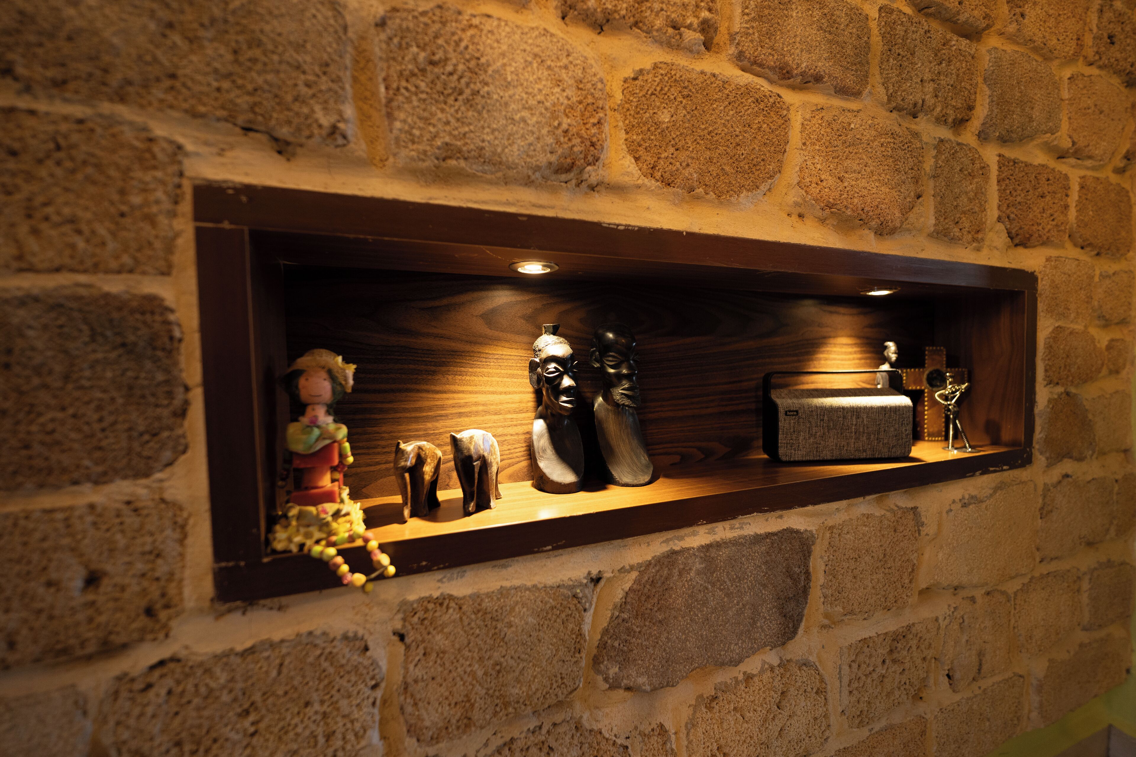 Una pared de piedra con un estante que exhibe varios objetos, incluyendo figuritas y una radio pequeña.