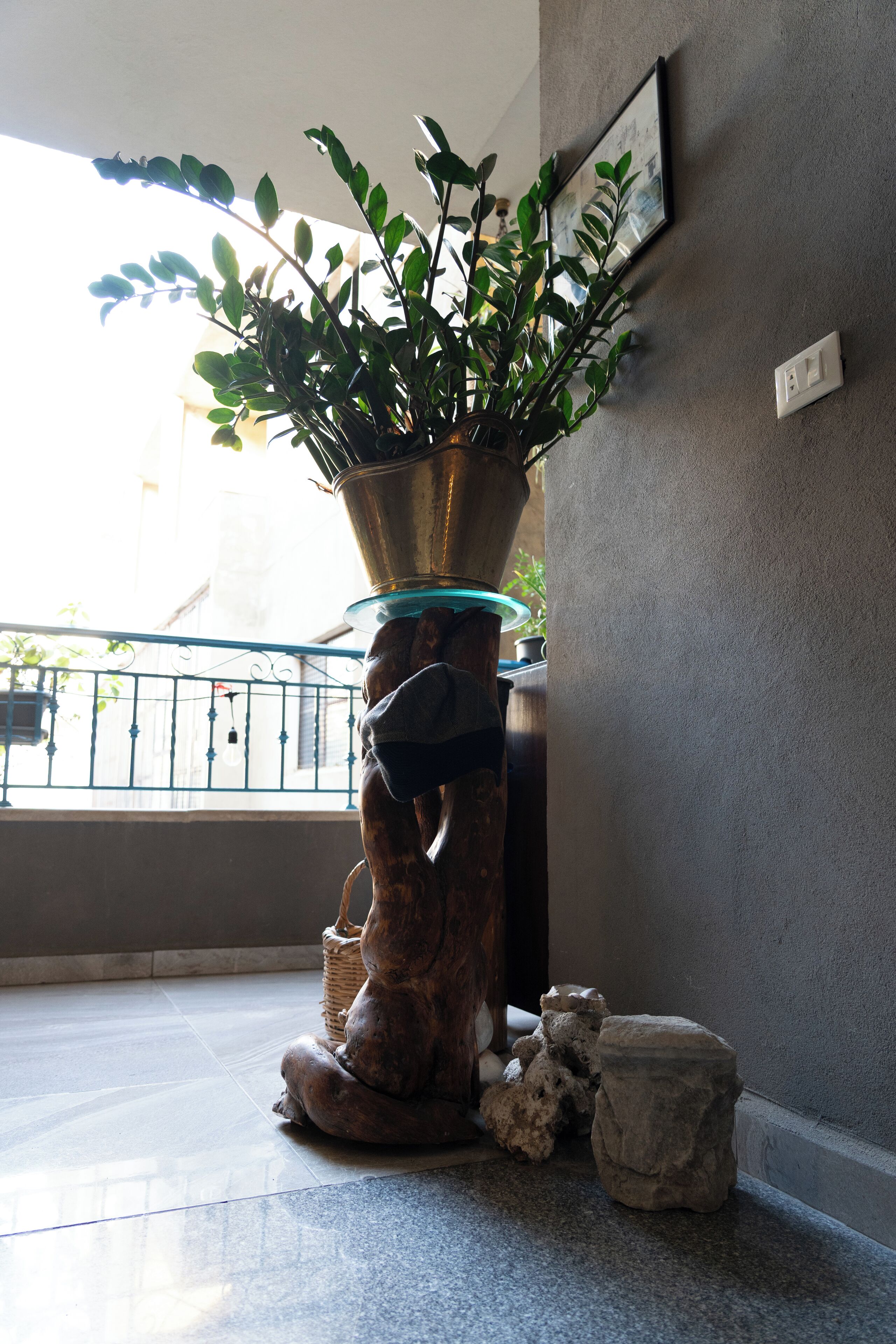 A potted plant on a pedestal in a room with a tiled floor and a balcony with a railing.