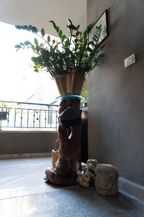 A potted plant on a pedestal in a room with a tiled floor and a balcony with a railing.