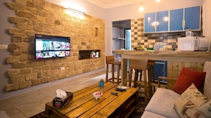 A living room with a stone wall, a TV mounted on it, a wooden coffee table, and a sofa with cushions. - InnTown (Tyre)