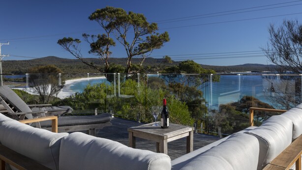 A terrace with a view of a beach and pool, furnished with a sofa, table, and lounge chairs. - Beach Side Bay Of Fires (Binalong Bay)