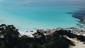 A coastal landscape with a clear view of turquoise waters, rocky shoreline, and dense greenery. - Beach Side Bay Of Fires (Binalong Bay)