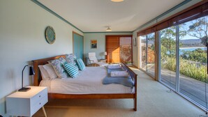 A bedroom with a large bed, a bedside table, a nightstand, a window with a view of the outdoors, and a ceiling light. - Beach Side Bay Of Fires (Binalong Bay)