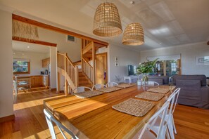 A spacious living area with a wooden dining table, white chairs, and a staircase leading to another level. - Montery By of Fires (Binalong Bay)