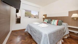 Una camera da letto con un letto, una finestra, una TV a schermo piatto e un comodino con una lampada.