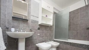 Un bagno con lavandino, due servizi igienici, uno specchio e una cabina doccia.