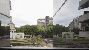 Vista attraverso una finestra di un edificio moderno, con il riflesso di un parco e di un grattacielo sullo sfondo.
