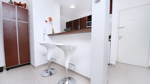 A modern kitchen with wooden cabinets, a white countertop, and two white bar stools. - Bvd. Illia Apartment AN4 (Córdoba)
