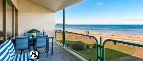 A balcony with a table and chairs, a striped cushion, and a view of the beach and ocean.