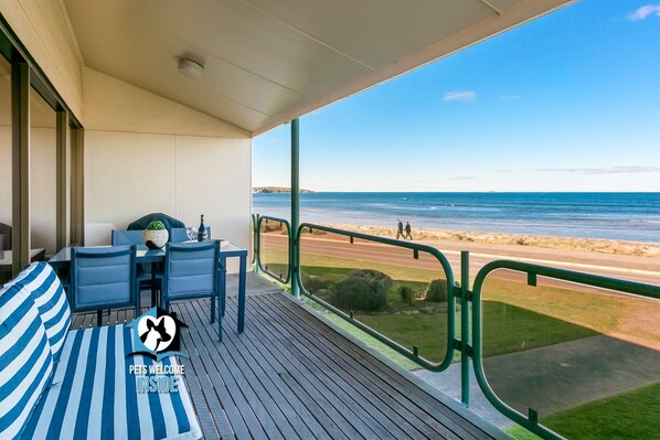 A balcony with a table and chairs, a striped cushion, and a view of the beach and ocean.