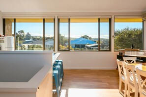 A modern kitchen with large windows, wooden flooring, and a dining area with a table and chairs.