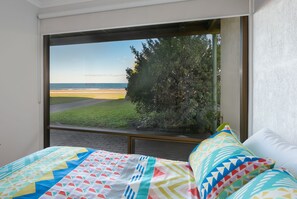 A bedroom with a large window overlooking a beach and a hedge.