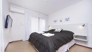 A modern hotel room with a large bed, a built-in shelf, and a window with curtains.