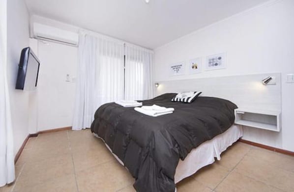 A modern hotel room with a large bed, a built-in shelf, and a window with curtains.