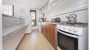 A kitchen with a gas stove, oven, and a kettle on the countertop.