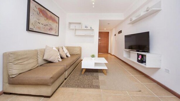 A modern living room with a beige sofa, a white coffee table, and a flat-screen TV mounted on the wall.