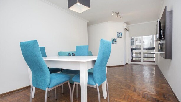 A dining area with a white table and blue chairs, a wooden herringbone floor, and a modern pendant light. - Obispo Salguero 21A (Córdoba)