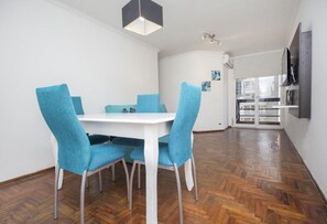A dining area with a white table and blue chairs, a wooden herringbone floor, and a modern pendant light. - Obispo Salguero 21A (Córdoba)
