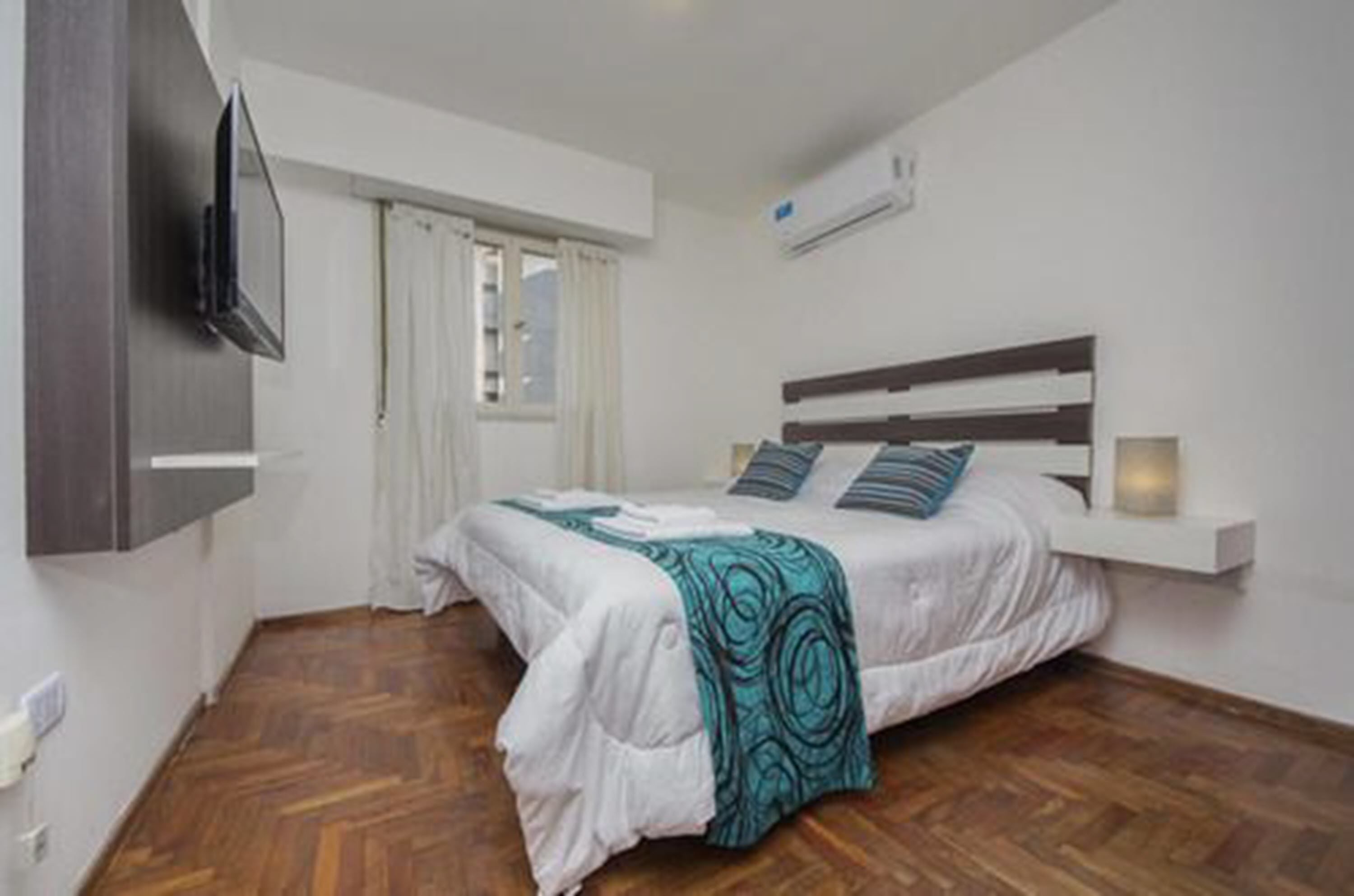 A bedroom with a bed, a TV mounted on the wall, and a window with curtains.