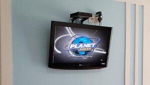 Un televisor montado en una pared azul claro con un logotipo que dice "PLANET SUKAN".