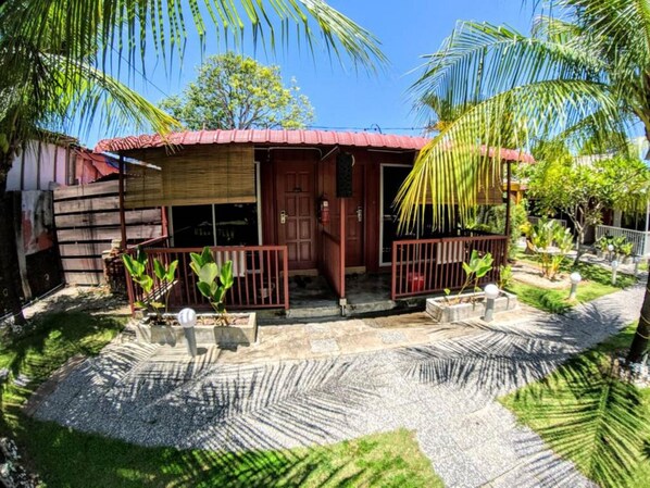 A two-story house with a red roof, a front porch, and a small garden area with palm trees and potted plants. - The Cabin Langkawi (Langkawi)