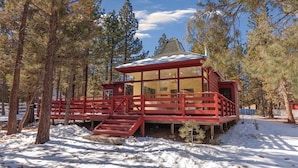Une cabane à l’extérieur rouge, dotée de grandes fenêtres et d’une terrasse en bois.