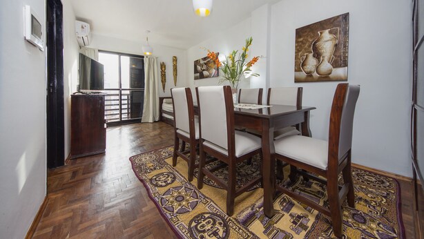 A dining area with a wooden table and chairs, a patterned rug, and a painting on the wall. - Dean Funes X22 (Córdoba)