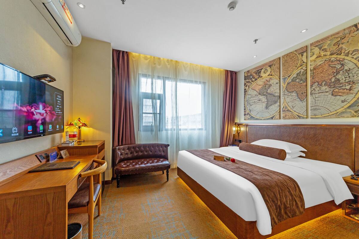 A hotel room with a large bed, a desk with a chair, a television, and a map on the wall.